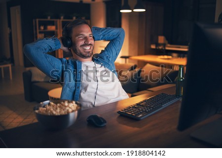 Cheerful handsome man sitting at his home office, watching funny show on computer and laughing