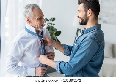 Cheerful Handsome Son Helping Elegant Retired Father Tying Blue Tie At Home 