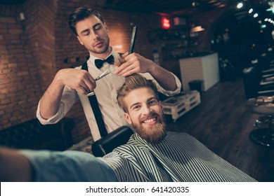 Cheerful handsome stylish red bearded guy with beaming smile is taking selfie at barber shop, stylish is making him a brand new haircut - Powered by Shutterstock