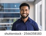 Cheerful handsome young African American businessman posing for head shot in office, looking at camera with toothy smile. Confident successful Black business leader man, startup manager portrait