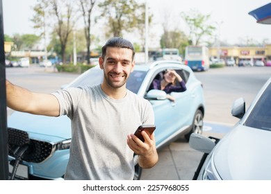 Cheerful happy Asian man using an EV charging application on smartphone to prepare vehicle charging and payment. Modern lifestyle of transportation with sustainability and sustainable energy. - Shutterstock ID 2257968055
