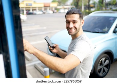 Cheerful happy Asian man using an EV charging application on smartphone to prepare vehicle charging and payment. Modern lifestyle of transportation with sustainability and sustainable energy. - Shutterstock ID 2257968059