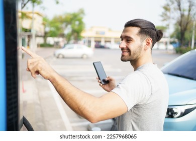 Cheerful happy Asian man using an EV charging application on smartphone to prepare vehicle charging and payment. Modern lifestyle of transportation with sustainability and sustainable energy. - Shutterstock ID 2257968065