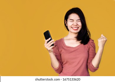 Cheerful Happy Asian Woman Get Good News Hand Holding Smart Phone Over Yellow Background  