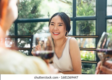 Cheerful happy asian woman on white dress enjoy party with friends, holding a wine glass, talking with friends.
