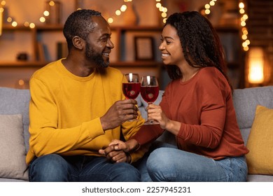 Cheerful happy beautiful loving african american couple relaxing together at home, smiling man and woman sitting on couch in cozy living room, drinking red wine, chatting, laughing - Powered by Shutterstock