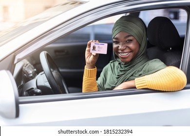 Cheerful Happy Black Muslim Woman In Hijab Sitting In Her Car And Showing New Driver License, Celebrating Driving School Finish, Passed Exam, Bought Car, Sitting Inside Of Vehicle, Looking From Window