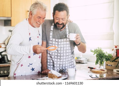 Cheerful And Happy Couple Father Son Middle Age And Senior Mature Cooking Cake Together At Home At The Kitchen. Using Sugar And Stuffs And Have Fun Working Together Creating Sweet Food. Bright Image 