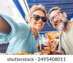 Cheerful happy couple take selfie picture together eating pizza at pizzeria restaurant in outdoor terrace. Happy tourist clients enjoying italian food and smiling at social media sharing moment