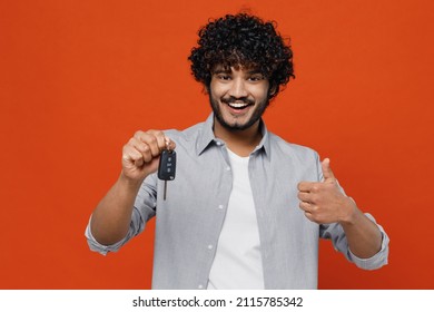 Cheerful happy excited vivid driver young bearded Indian man 20s years old wears blue shirt hold in hand new car key showing thumb up like gesture isolated on plain orange background studio portrait