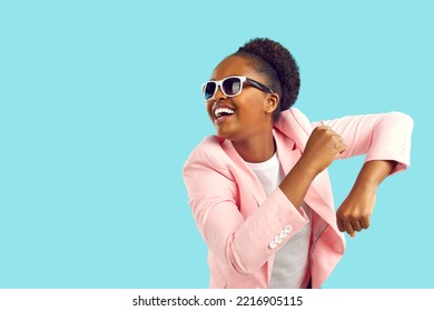 Cheerful happy excited young African American girl in pink suit and sunglasses dancing and having fun. Portrait of funny woman dressed up for party dancing isolated on bright blue copyspace background - Shutterstock ID 2216905115