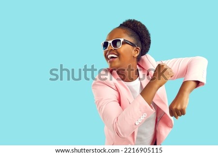 Cheerful happy excited young African American girl in pink suit and sunglasses dancing and having fun. Portrait of funny woman dressed up for party dancing isolated on bright blue copyspace background
