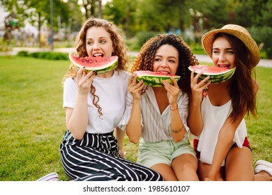 Cheerful Happy Friends Camping On The Grass, Eating Watermelon, Laughing. Three Young Woman Relaxing And Enjoying Holidays Together. People, Lifestyle, Travel, Nature And Vacations Concept.