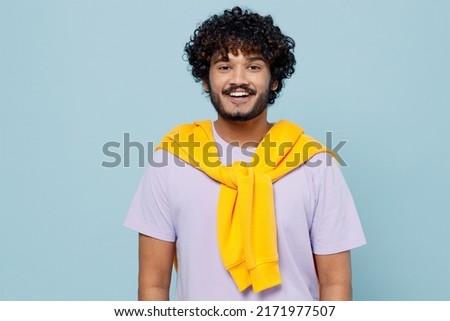 Cheerful happy fun stunning young bearded Indian man 20s years old wears white t-shirt looking camera isolated on plain pastel light blue background studio portrait. People emotions lifestyle concept