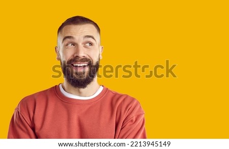 Cheerful happy funny joyful bearded young man in sweatshirt isolated on solid yellow color background looking to blank empty copy space side and smiling