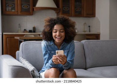 Cheerful Happy Gen Z Teen Girl Receiving Exciting Message On Smartphone, Reading Text In Screen, Smiling, Laughing, Sitting On Couch, Using Online Virtual App On Mobile Phone