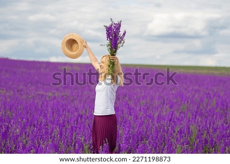 Cheerful happy girl in a flowering lilac field with a bouquet and a hat in her hands.