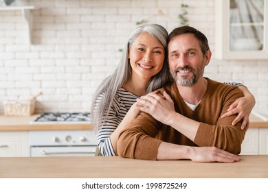 Cheerful happy mature middle-aged caucasian couple family parents husband and wife emracing hugging, spending time together in the kitchen at home, sharing love and care. Social distance concept