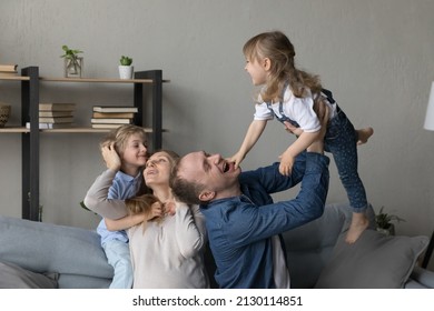 Cheerful Happy Parents Cuddling, Tickling Excited Giggling Little Preschool Kids On Couch. Dad And Expecting Mother Playing Active Games With Sibling Children, Enjoying Family Leisure Time At Home.