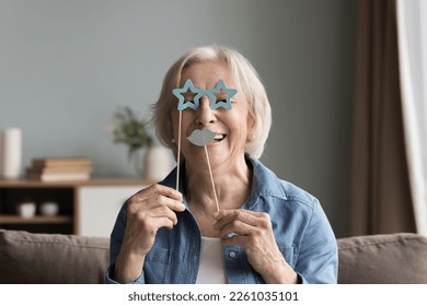 Cheerful happy senior woman applying fake paper moustache and goggles on stick to face, looking at camera, having fun, smiling, laughing, using prop for photo shooting - Powered by Shutterstock