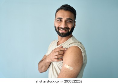 Cheerful Happy Smiling Indian Man Standing With Plaster On Shoulder After Getting Covid 19 Vaccine Isolated On Blue Background. Coronavirus Vaccination Campaign Concept. Copy Space. Portrait.