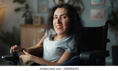 Cheerful happy woman with disability sitting in a motorized wheelchair at cozy home in free time smiling and looking at the camera and smiling