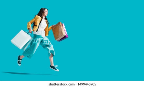 Cheerful happy woman enjoying shopping: she is carrying shopping bags and running to get the latest offers at the shopping center - Shutterstock ID 1499445905