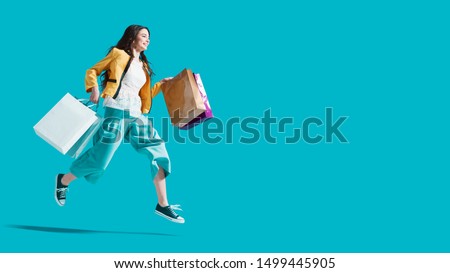 Cheerful happy woman enjoying shopping: she is carrying shopping bags and running to get the latest offers at the shopping center