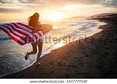 Cheerful happy woman outdoors on the beach holding USA flag having fun.