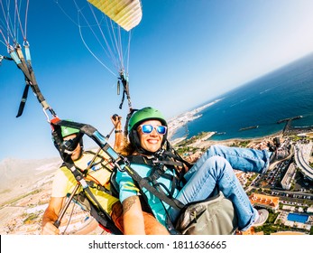 Cheerful happy woman to paraglyde experience with pilot - couple having fun in the air paraglyding over the city with coastline view - tourist and summer holiday vacation active people