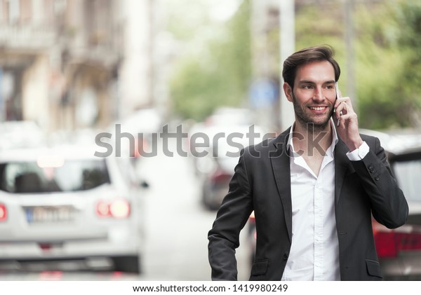 Cheerful happy young\
business man enjoying a nice talk over his phone, walking the\
streets of a city