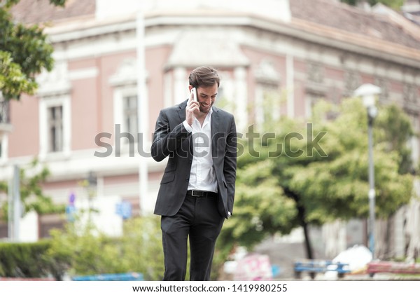 Cheerful happy young\
business man enjoying a nice talk over his phone, walking the\
streets of a city