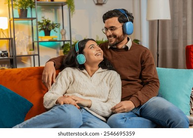 Cheerful happy young diverse couple in wireless headphones dancing on couch at home listening favorite energetic disco rock n roll music. Smiling relaxed family enjoying weekend together in apartment. - Powered by Shutterstock