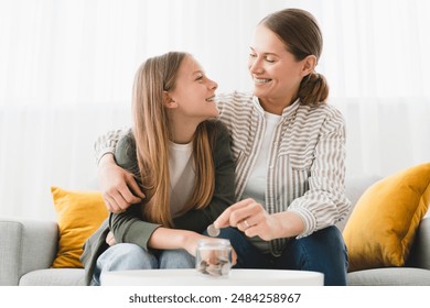 Cheerful happy young family of mother mom and daughter saving money, putting coins in bank, planning future, paying bills, loan. Nest egg concept. - Powered by Shutterstock