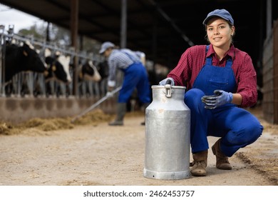 Cheerful hardworking woman farmer carrying milk can while walking through cow house in autumn - Powered by Shutterstock