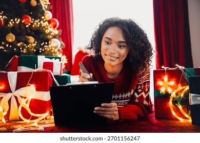 Cheerful helper writes notes by the Christmas tree as gifts glow with warm lights and festive cozy holiday magic and joy