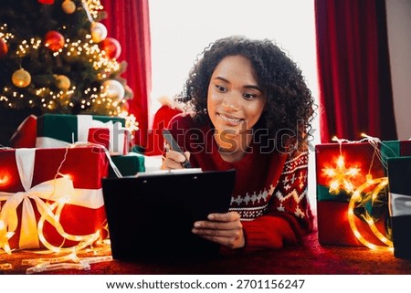 Cheerful helper writes notes by the Christmas tree as gifts glow with warm lights and festive cozy holiday magic and joy