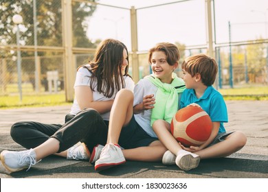 Cheerful high school students sit on the basketball court, relax after the game, talk and laugh. Sports, games, and education. The concept of friendship - Powered by Shutterstock