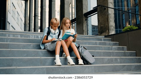 Cheerful high school students sitting on stairs street outdoors near campus talking smiling before classes. Caucasian boy and girl writing in their copybooks having an outdoor together after lessons - Powered by Shutterstock