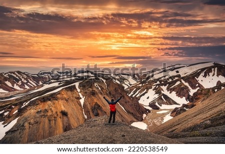 Cheerful hiker woman standing on the peak with volcanic mountain range with snow covered on Blanhjukur trail in summer at Landmannalaugar, Iceland