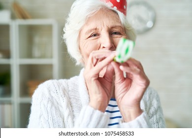 Cheerful Hilarious Elderly Woman With Wrinkles Having Fun Alone And Blowing Party Horn While Celebrating Party At Home