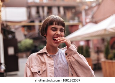 Cheerful hipster with short hair in light denim jacket laughing outdoors. Humored brunette girl with beige outfit has fun in city.. - Powered by Shutterstock