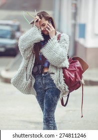 Cheerful Hipster Tourist Woman Talking On The Phone In The Street Wearing A Gray Stylish Coat, Keep Sunglasses In Hand . Fashion Street Style.