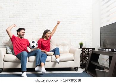 Cheerful Hispanic Boyfriend And Girlfriend Watching Soccer Match On TV At Home