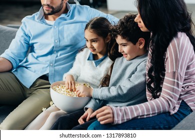 Cheerful Hispanic Family Watching Tv With Popcorn Bowl At Home