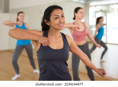 Cheerful hispanic woman practicing vigorous lindy hop movements in group dance class.