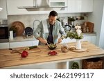 A cheerful home male chef mixing a bowl of fresh and healthy vegetable salad on a kitchen counter.