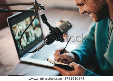 Cheerful host streaming his audio podcast using microphone and laptop at his small broadcast studio