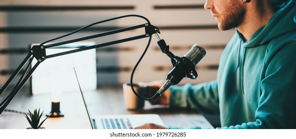 Cheerful host with stubble streaming his audio podcast using microphone and laptop at his small broadcast studio