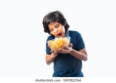 Cheerful Indian Asian Kid Boy Eating Potato Chips Or Wafers In A Bowl,  Standing Isolated Against White Background